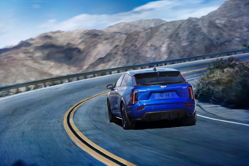 Rear View of a Blue 2026 OPTIQ-V Driving on a Curve of a Mountain Row | Sarant Cadillac in Farmingdale NY
